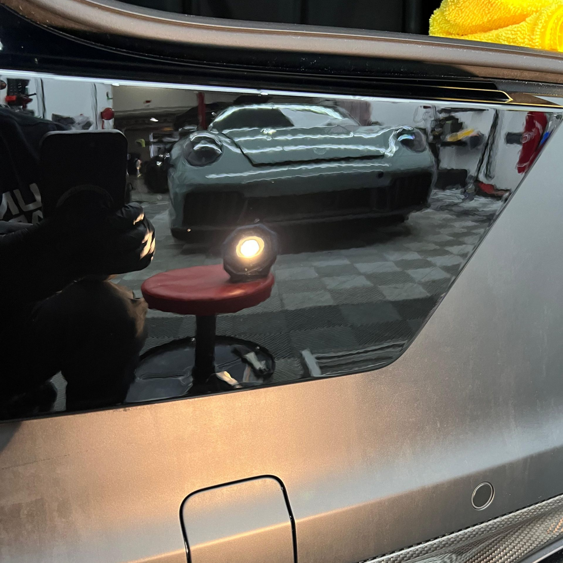 Close-up of a shiny green car body panel with a bright reflection and a small circular sensor near the bottom