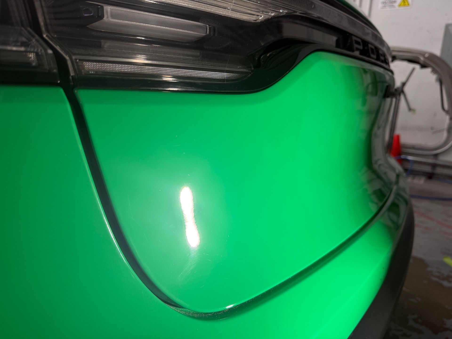 Green sports car front fender and headlight close-up in a garage