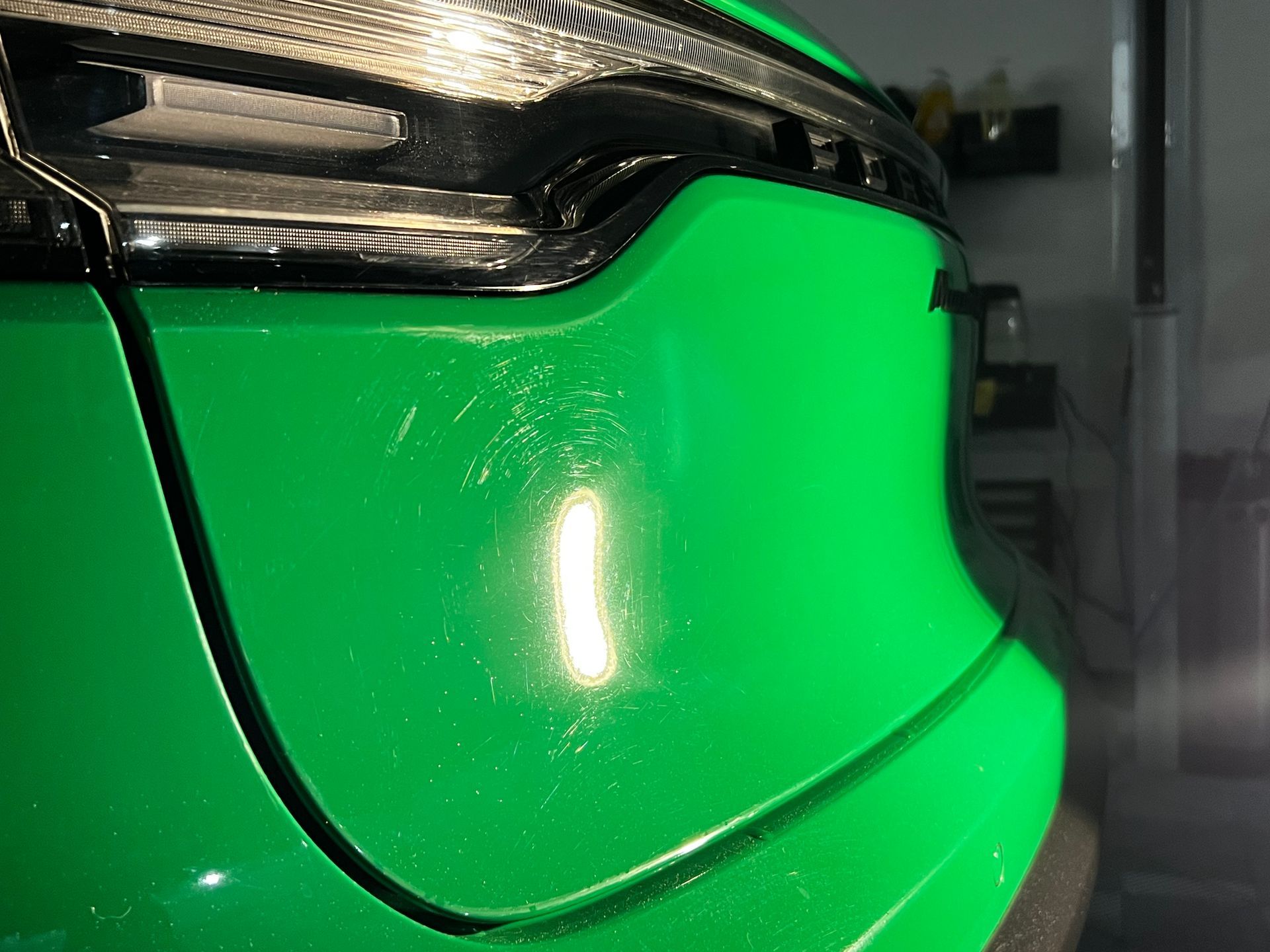Close-up of a bright green car front bumper and headlight with reflective paint.