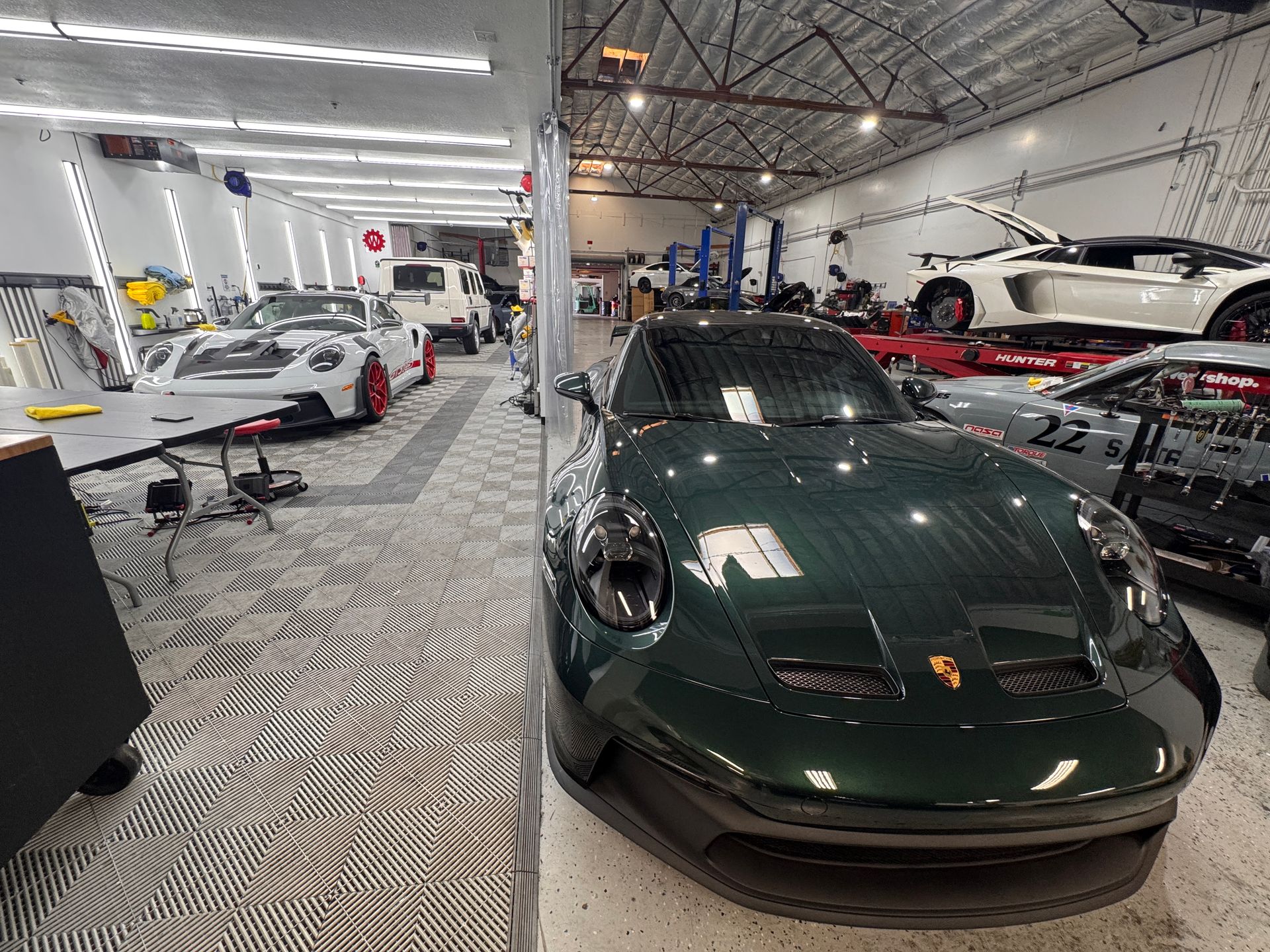 Luxury sports cars displayed inside an indoor showroom, including a dark green Porsche in the foreground.