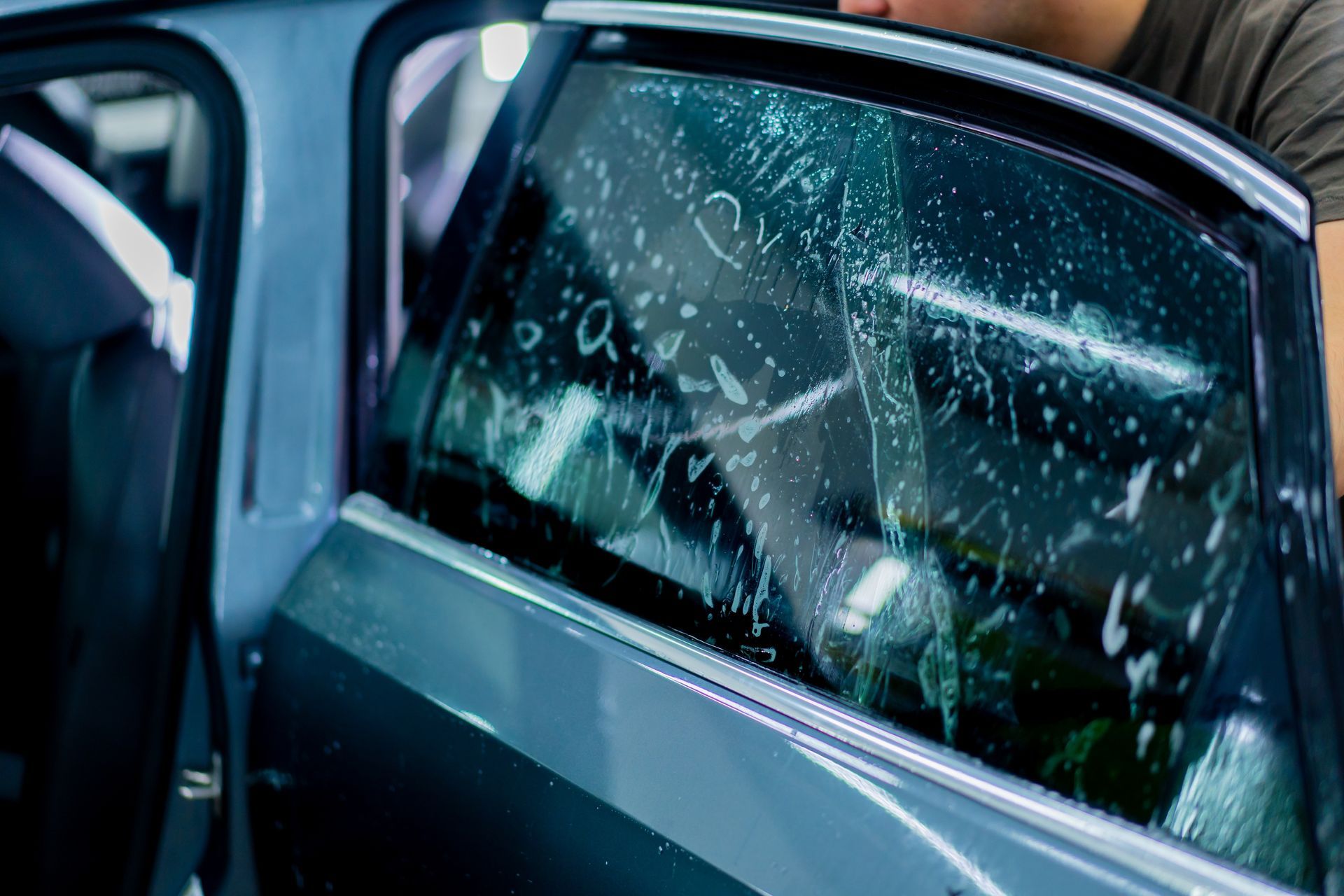 Blue car door window shattered with broken glass and rain droplets.