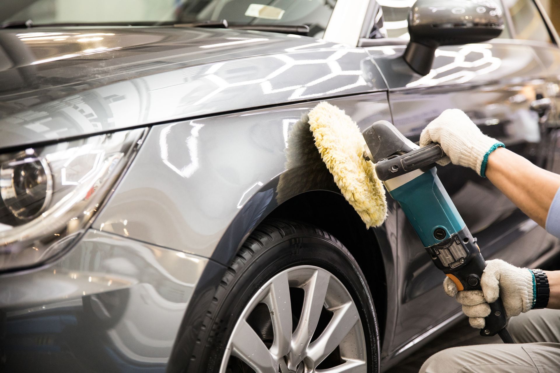 Detailing worker polishing a gray car fender with a buffer tool