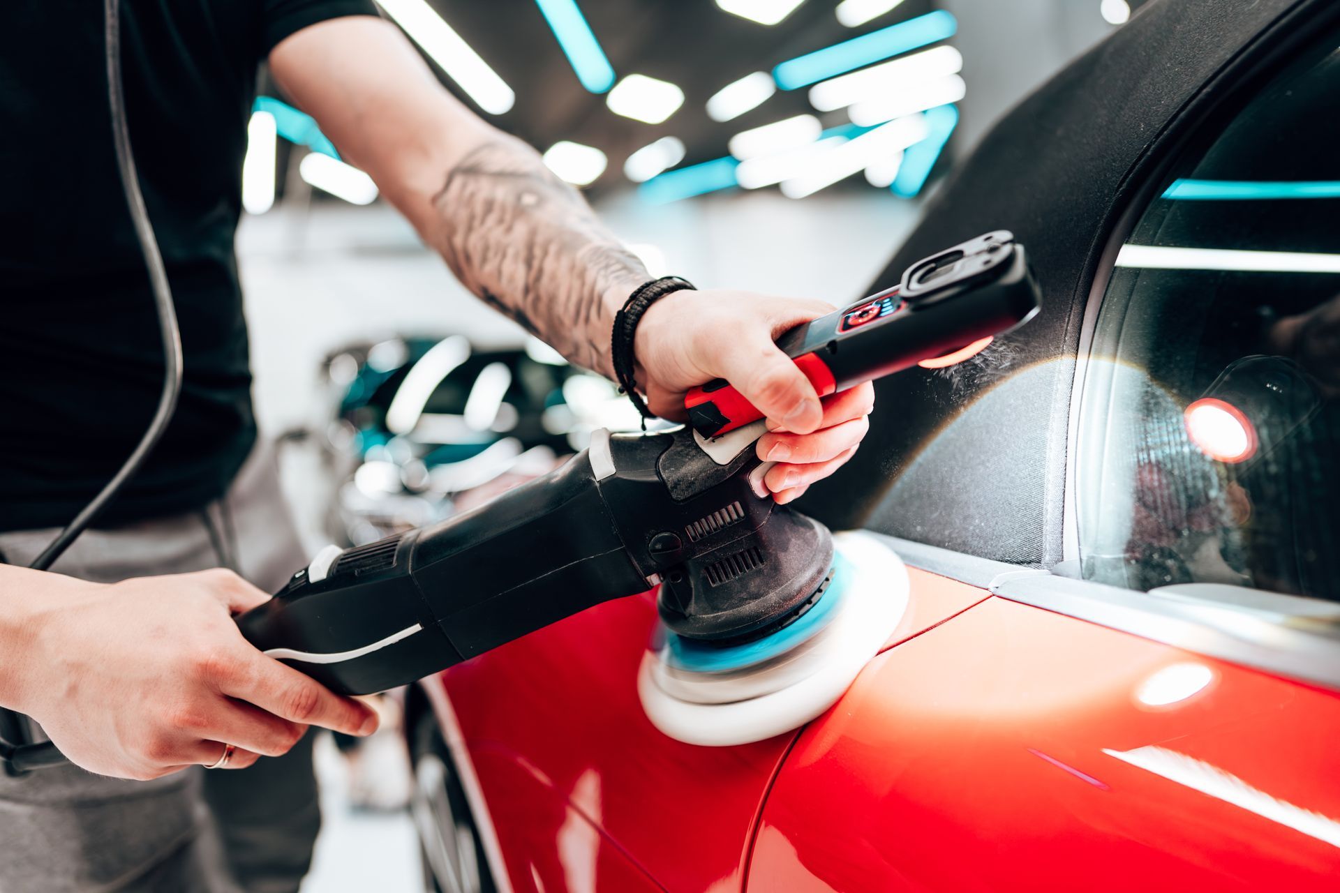 Hands polishing a red car with a buffer in a garage