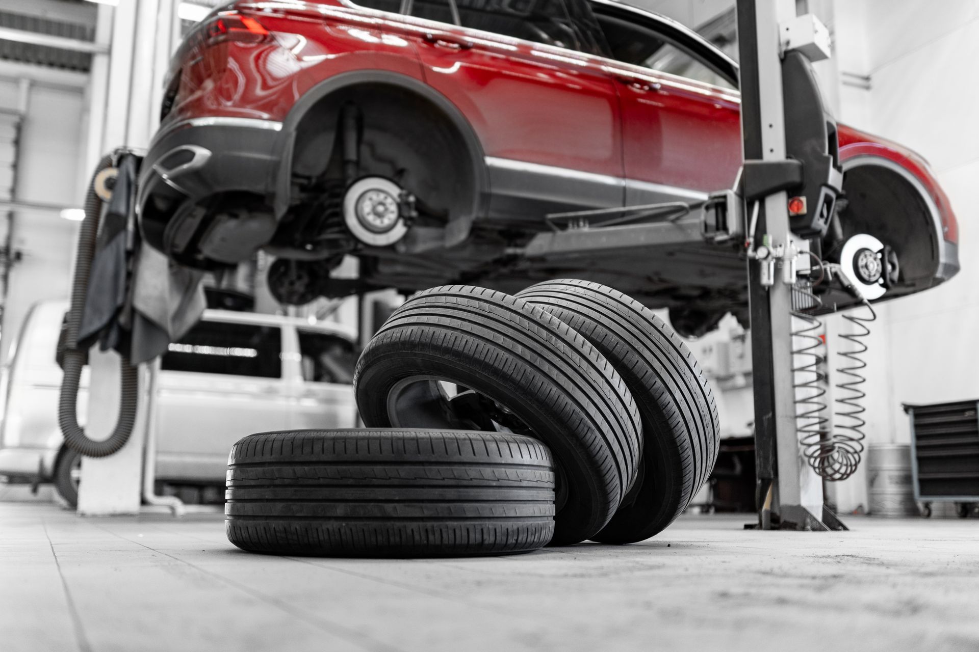 Red car lifted in a garage with stacked tires below and a mechanic working underneath