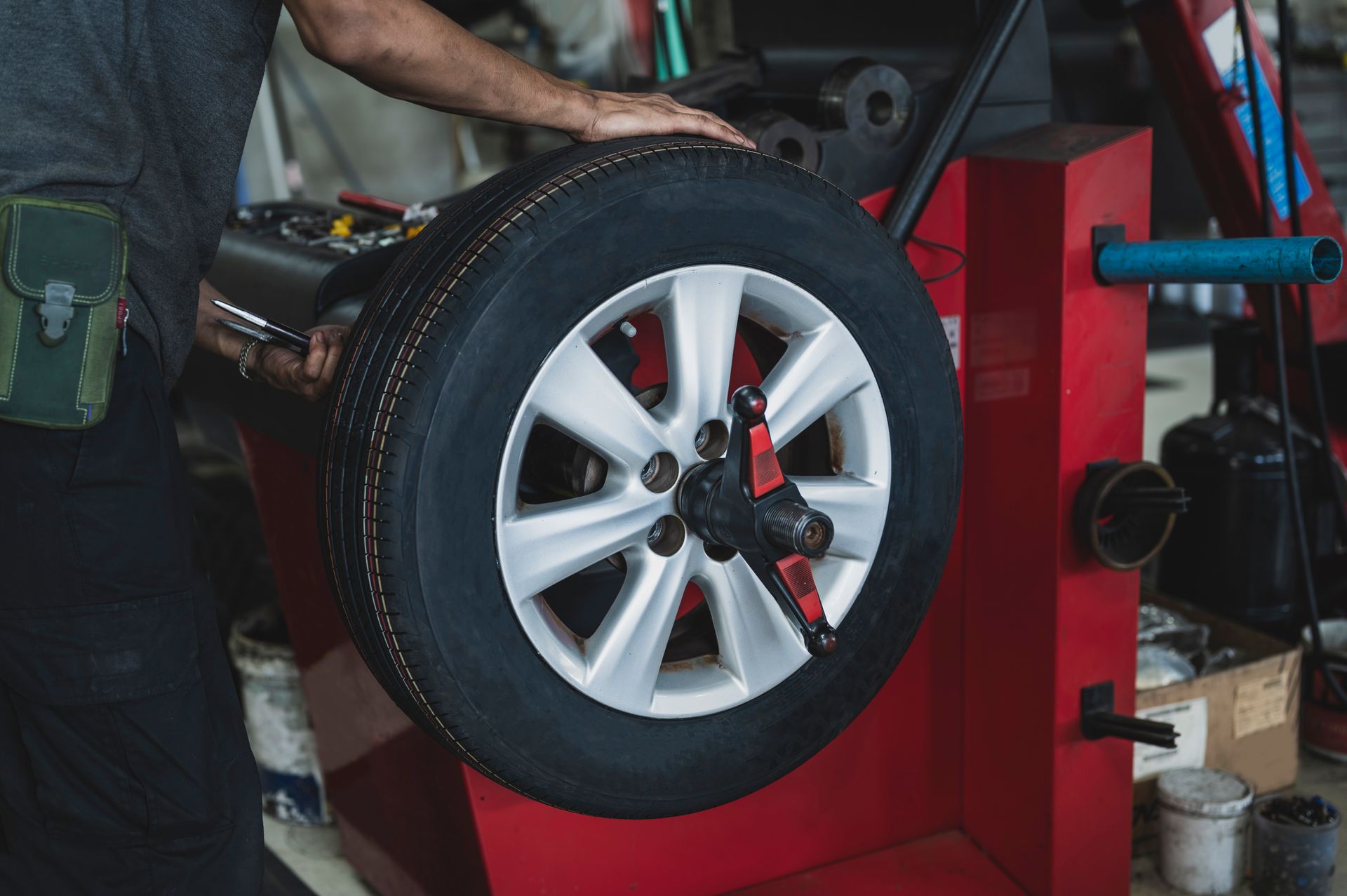 Car tire mounted on a wheel balancer in an auto repair shop, with a mechanic working nearby