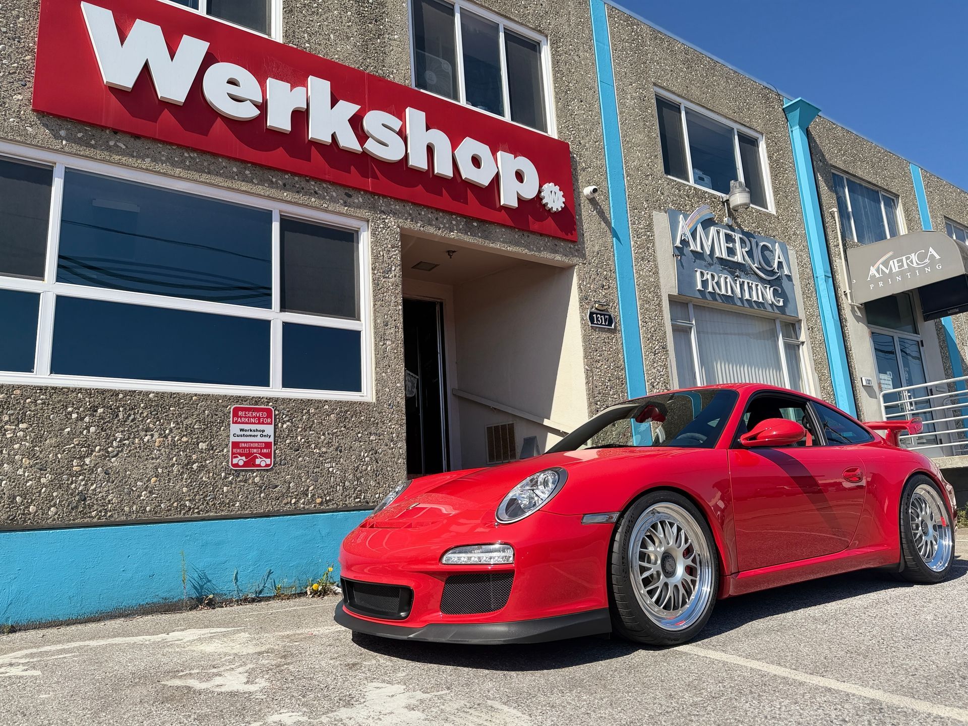 Red Porsche parked outside a workshop with a large red “Werkshop.” sign above the entrance