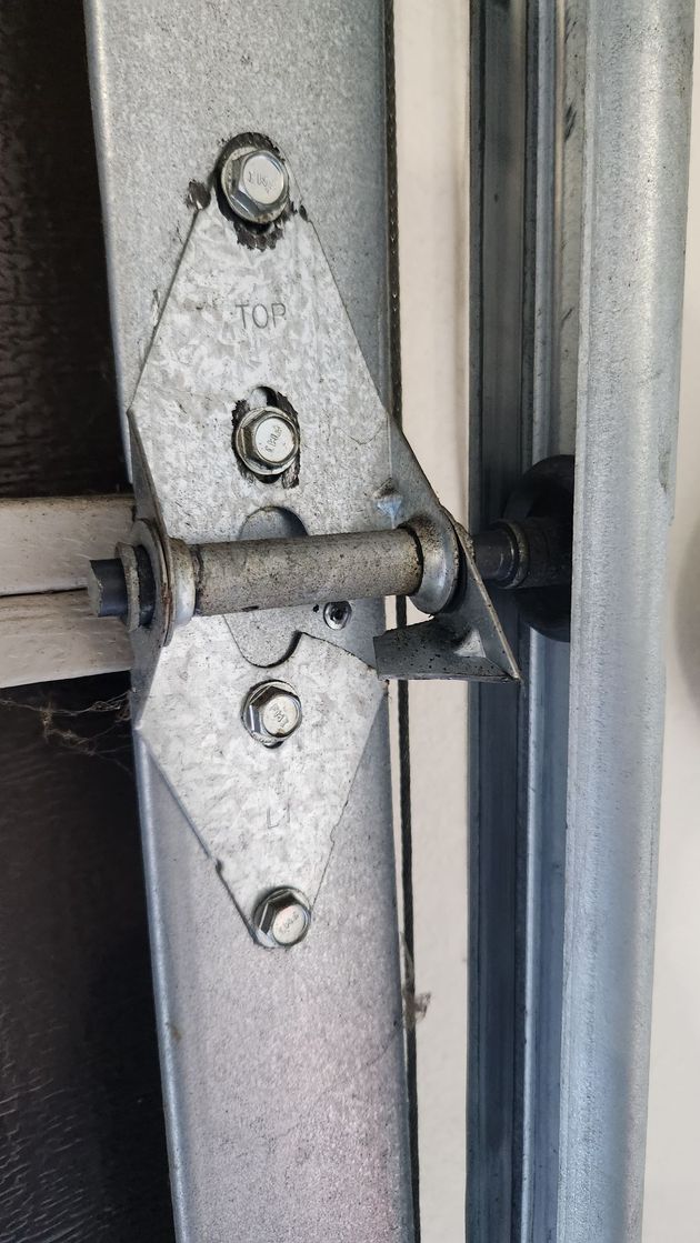 Technician lubricating garage door rollers and hardware during routine maintenance