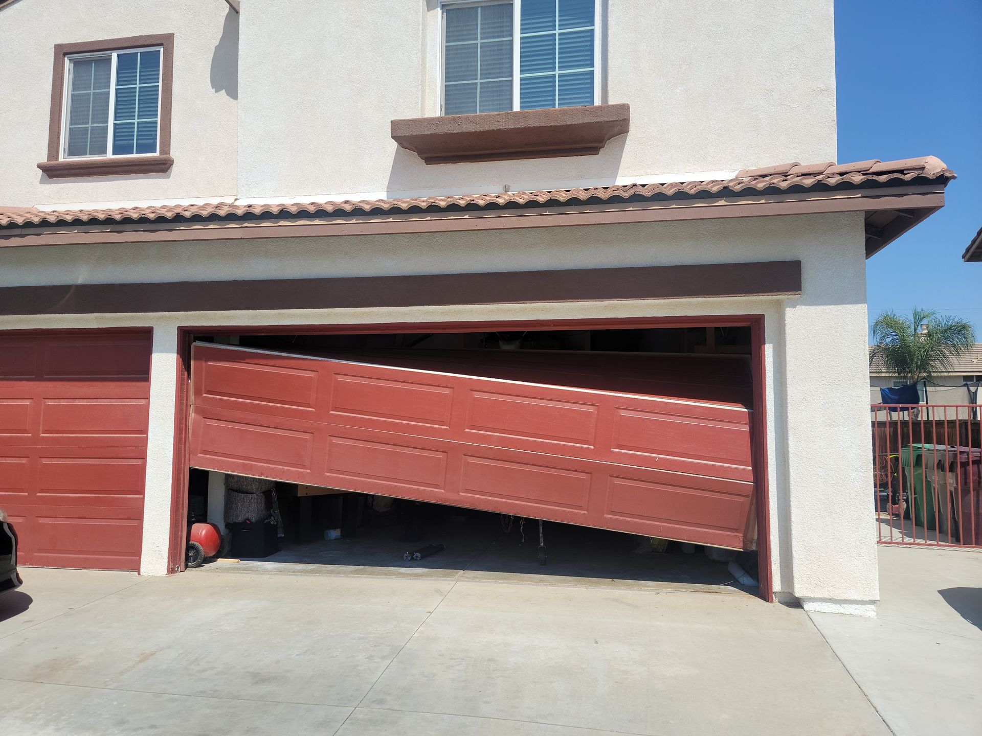 Tilted red garage door on a house, partially open with a car parked inside.