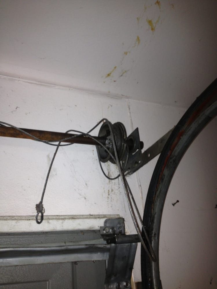 Close-up of a wall-mounted cable pulley and wires near a garage door frame
