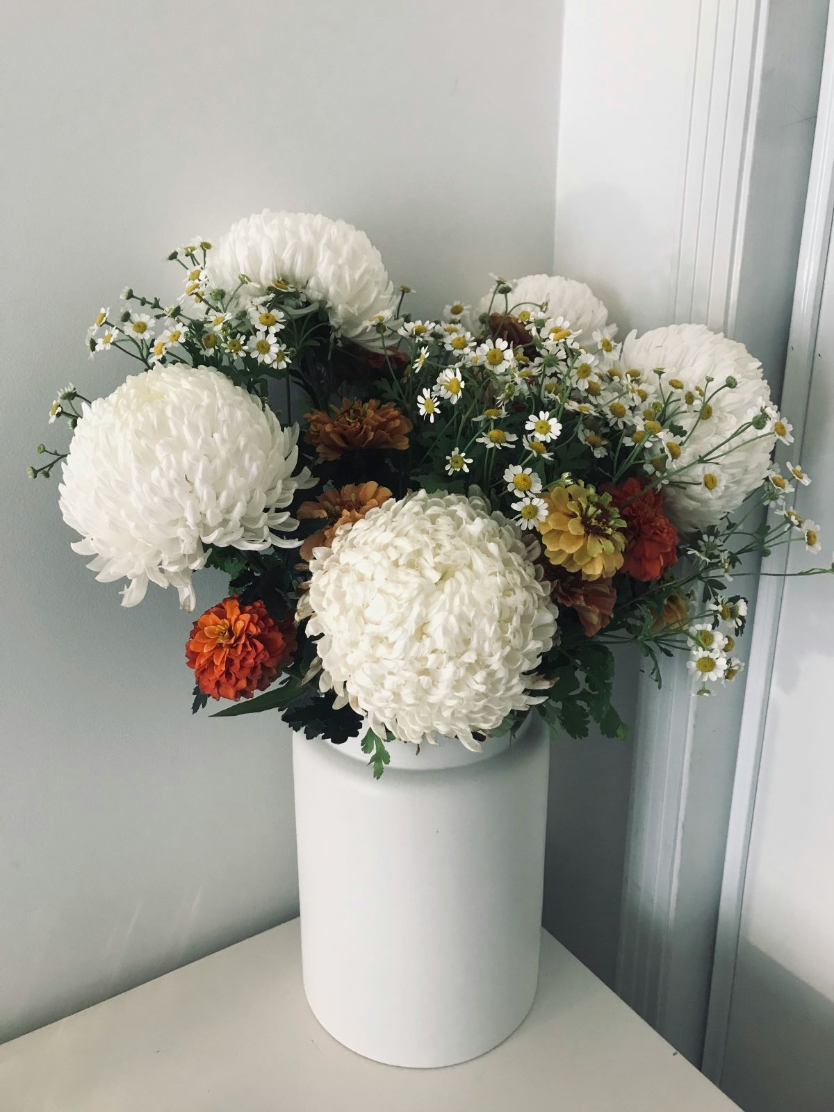 A white vase filled with white flowers is sitting on a table.