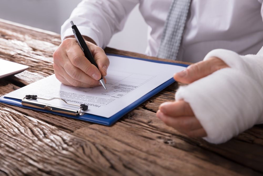 Person With Bandaged Wrist Writing on a Clipboard at a Wooden Desk — Dwyer Law Group in Surfers Paradise, QLD