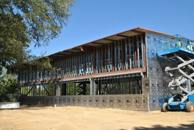 Modern building under construction with exposed framing, metal scaffolding, and a blue boom lift outside