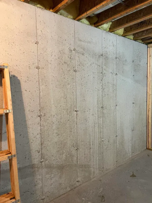 Unfinished concrete basement wall with exposed ceiling joists and wooden support posts