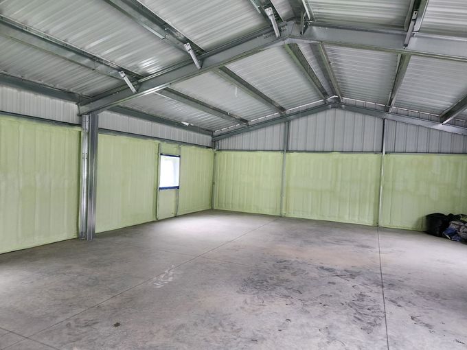 Empty metal warehouse interior with green walls, corrugated roof, and concrete floor