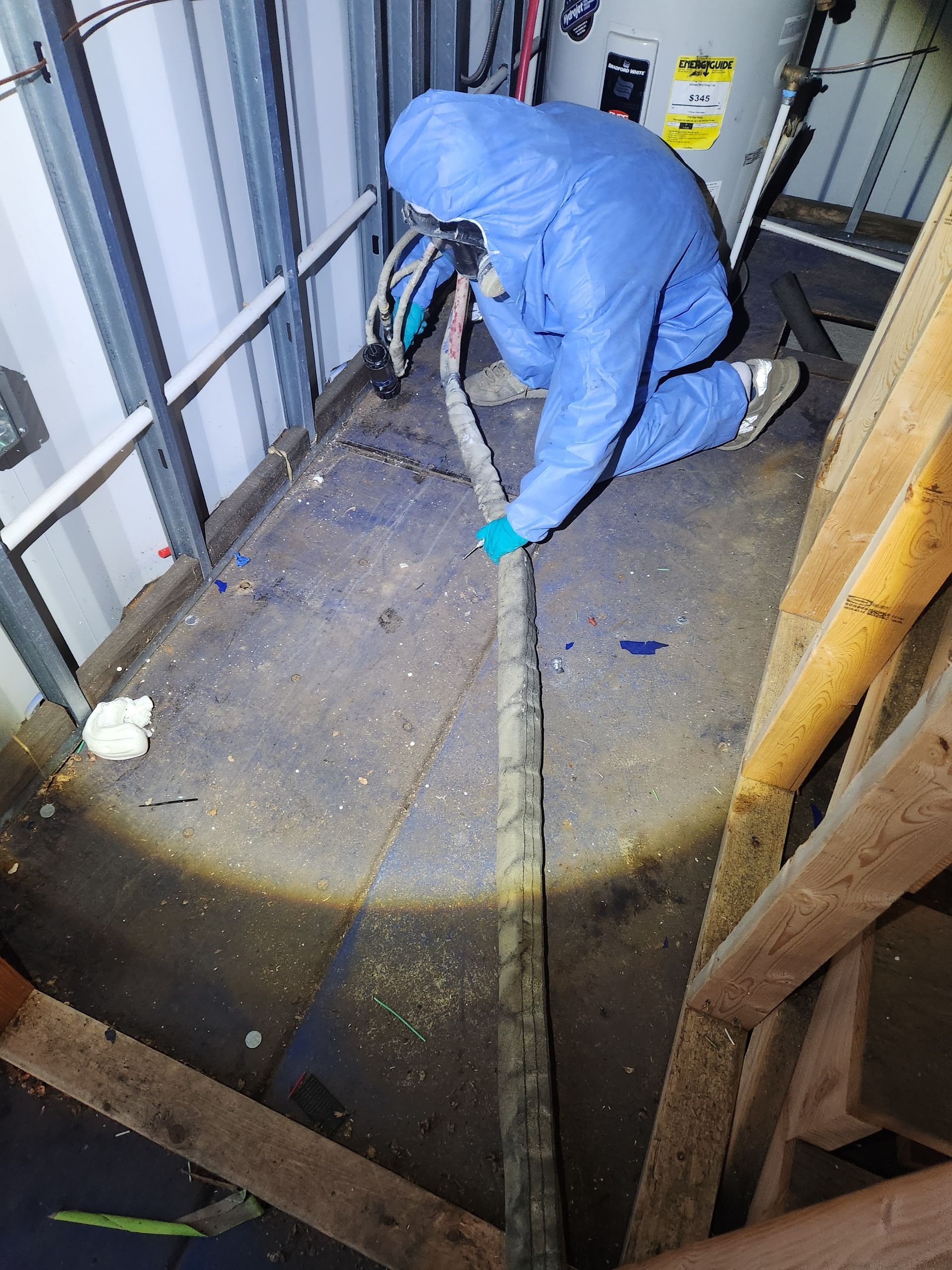 Worker in blue protective gear kneeling and cutting a floor opening with a power saw in a narrow industrial space