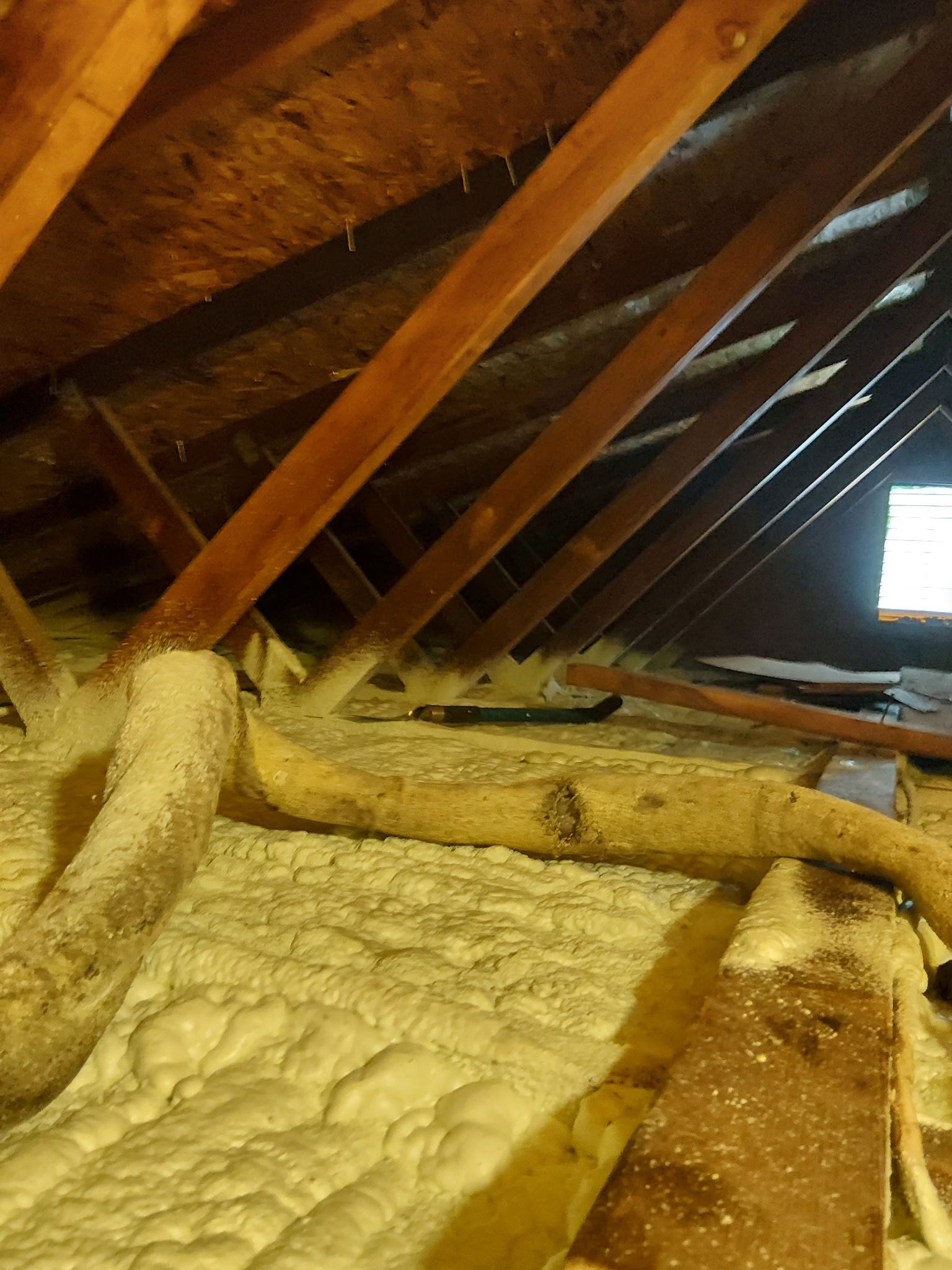 Insulated attic with wooden rafters and beams, lit by a small window