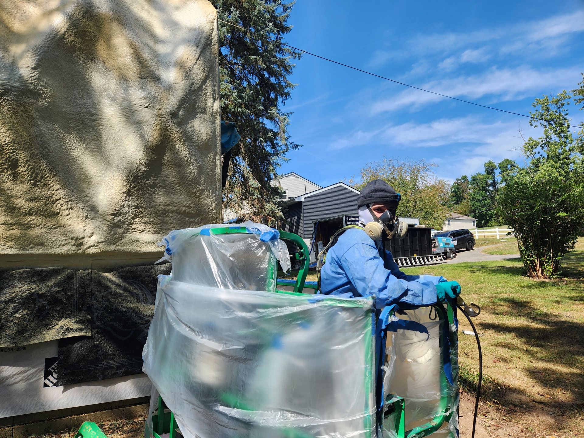 Worker in blue protective gear spraying liquid onto a large tank outdoors on a sunny day