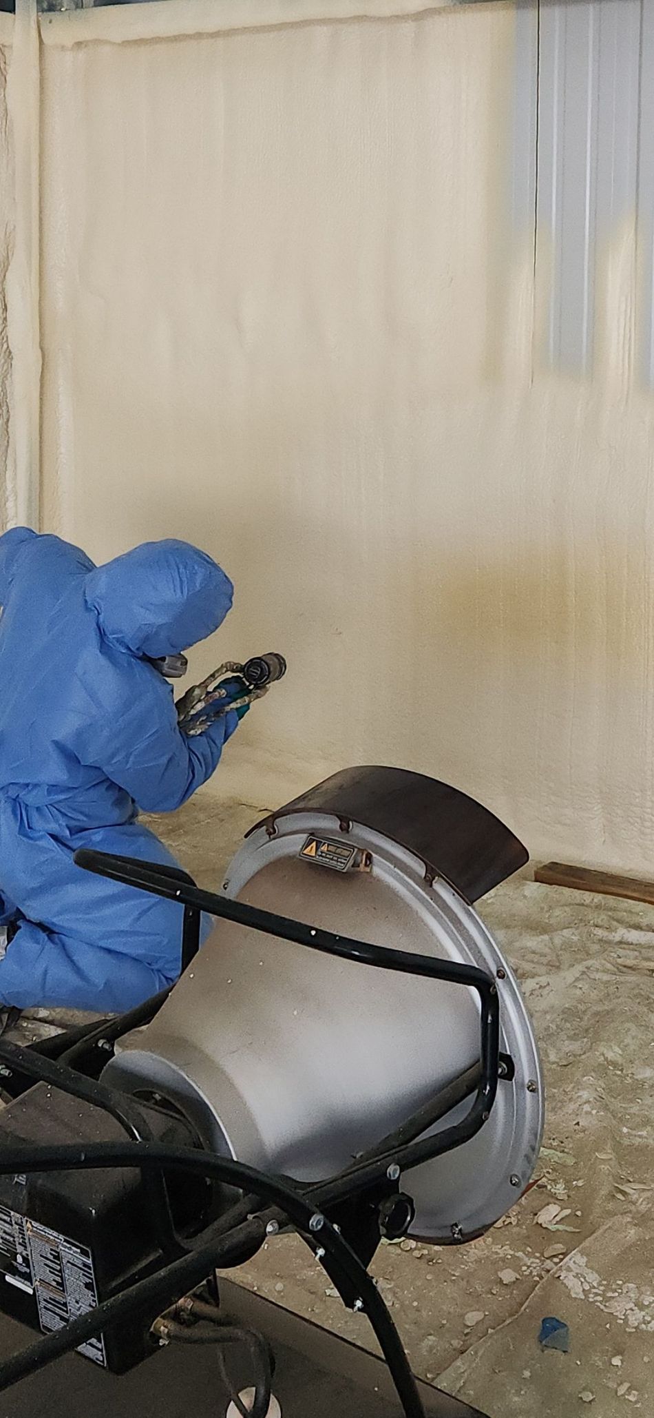 Blue-gloved hand holding a metal tool near a silver machine against a beige wall