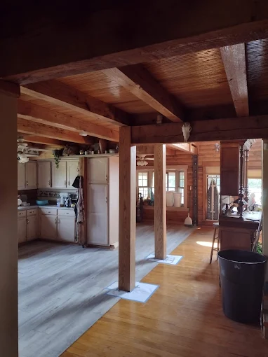 Rustic open-plan cabin interior with wood beams, kitchen, and sunlight on the floor