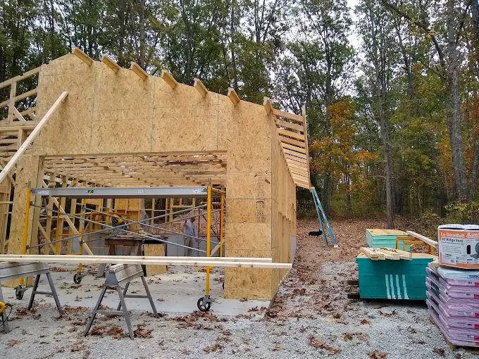 Partially built wooden house framed with scaffolding and construction materials in a wooded area