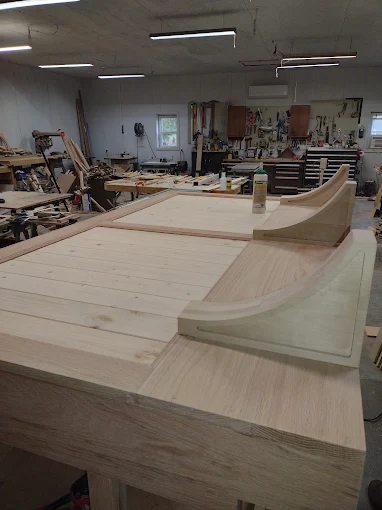 Wooden boat hull under construction in a workshop with tools and workbenches.