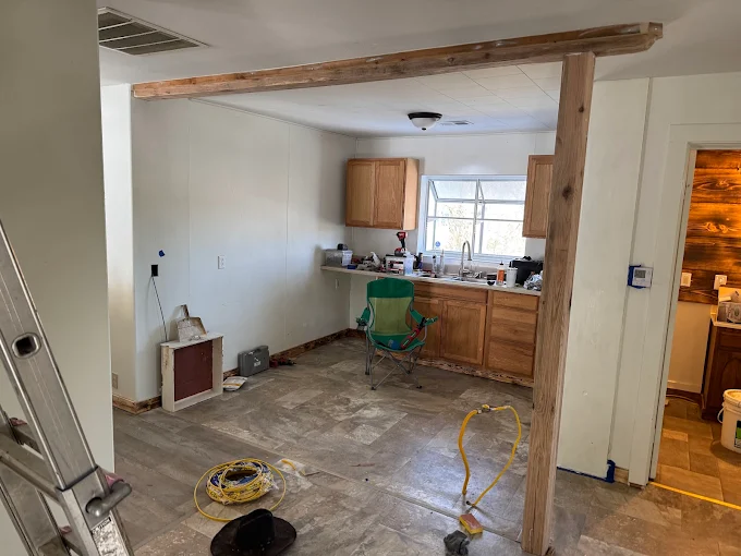 Kitchen under renovation with exposed subfloor, cabinets, tools, and a ladder in the foreground