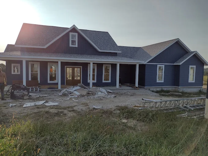 Blue house under construction with unfinished front yard and debris, seen in daylight