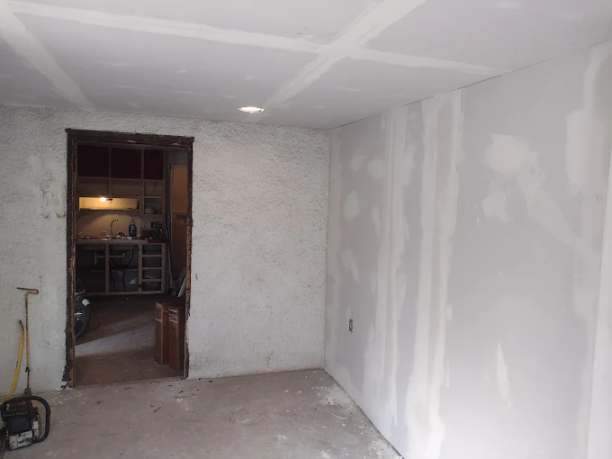 Empty unfinished room with white drywall, exposed doorway, and a concrete floor.