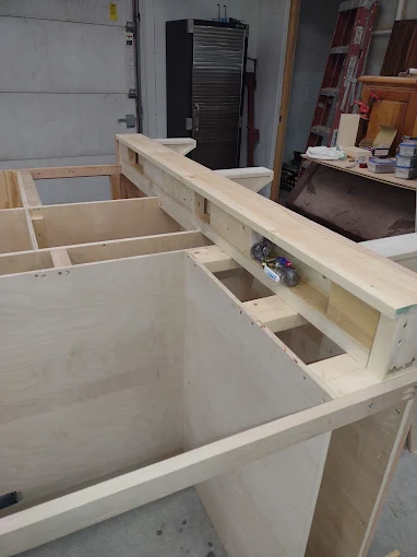 Wooden frame and plywood panels in a workshop, with a long beam and tools in the background