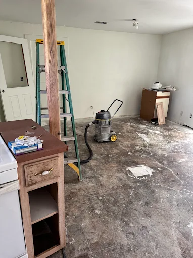 Dusty room under renovation with ladder, wet/dry vacuum, and scattered tools on bare floor