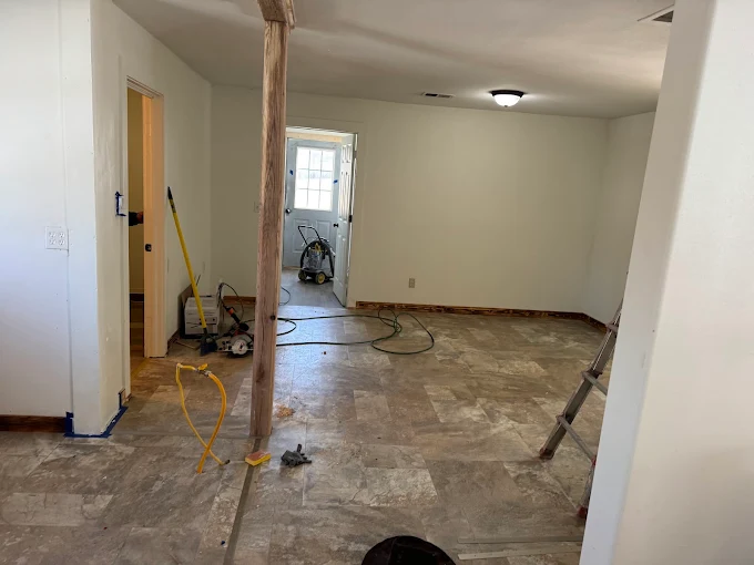 Unfinished room with exposed studs, concrete floor, and construction tools during renovation.