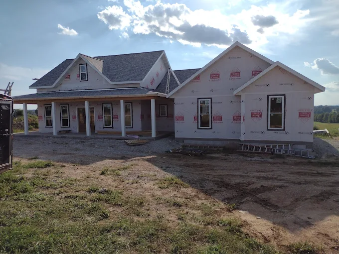 Single-story house under construction with white siding and a covered front porch on a bare lot.