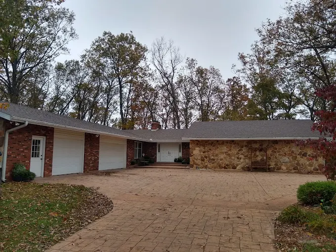 Brick house exterior with curved driveway and garage, surrounded by trees
