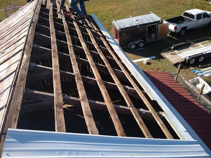Roof under repair with exposed rafters and workers near a white truck and trailer below