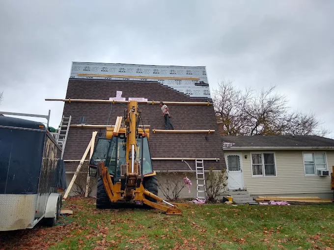 Construction crew working on a brick house with scaffolding, lift, and a ladder beside a small home