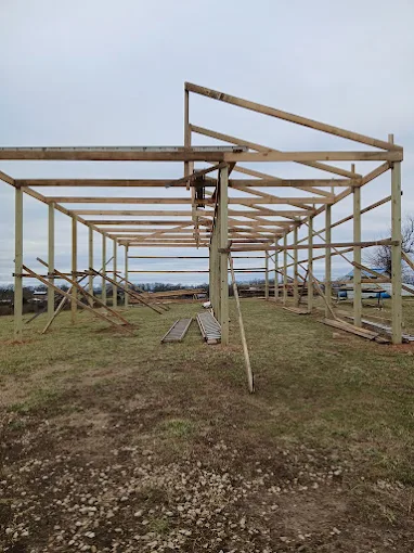 Partially built wooden frame structure on a grassy, open lot under cloudy sky