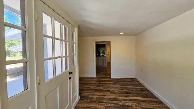 Empty hallway with white walls, wood-pattern floor, and front door with glass panes.