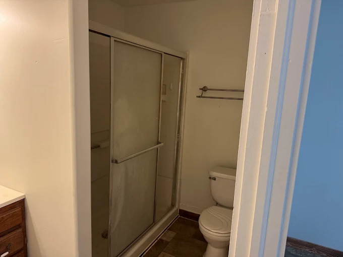 Small bathroom with a glass shower stall, toilet, and towel rack next to a doorway.