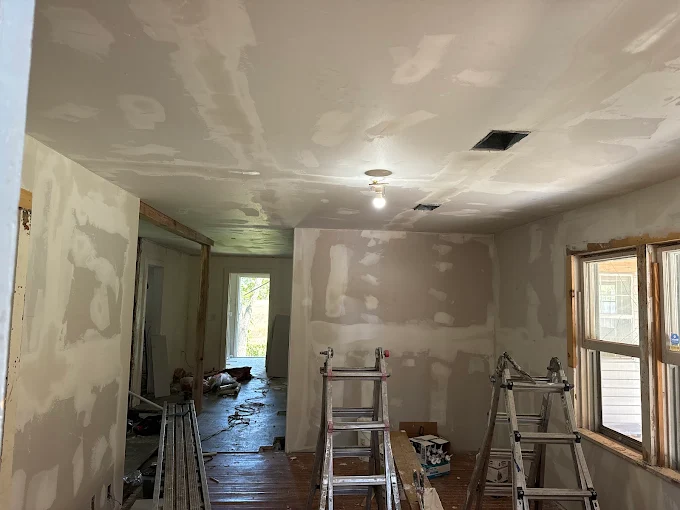 Partially renovated room with drywall, ladders, tools, and a window on the right