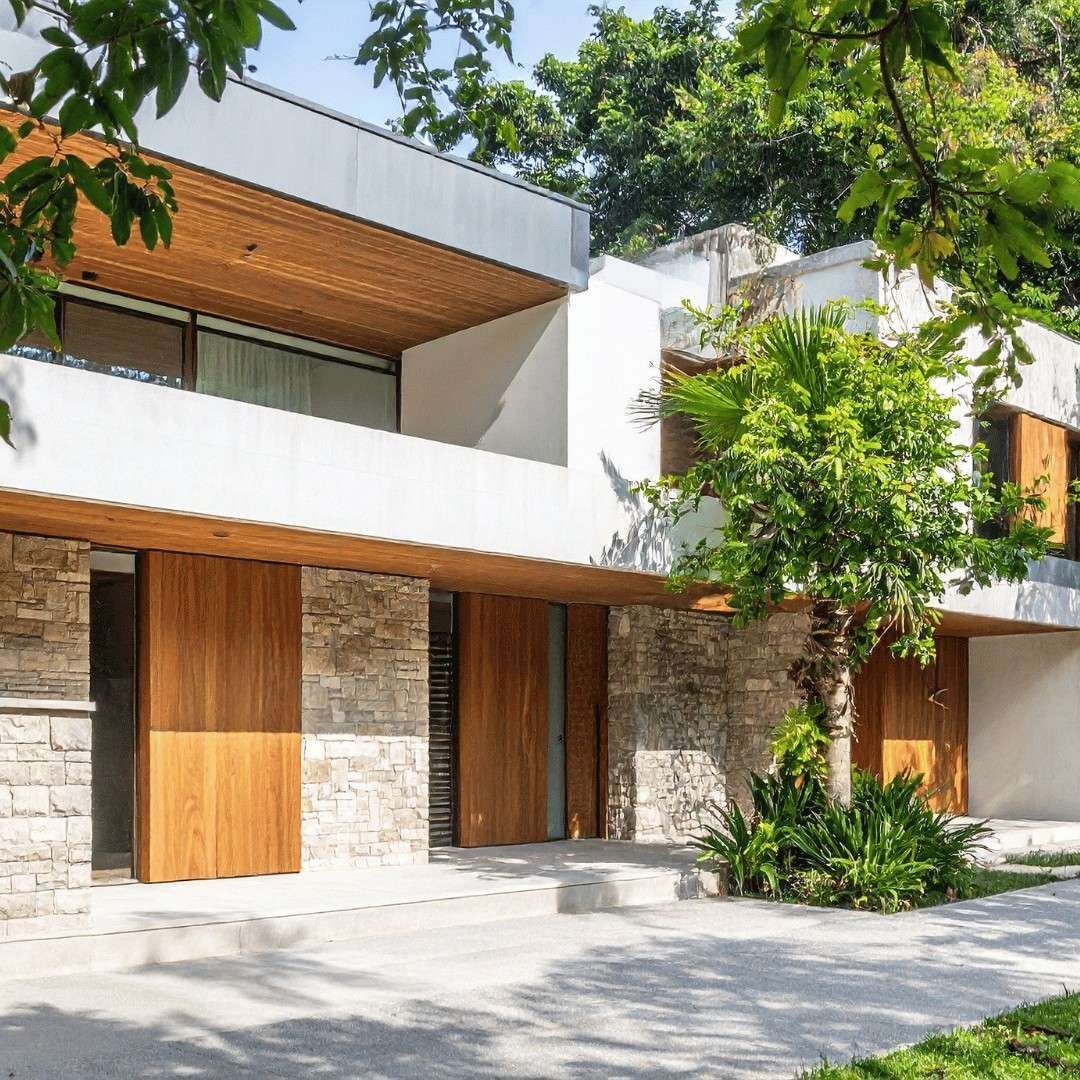 Modern stone-and-wood townhouse facade with balconies, large windows, and leafy trees in front