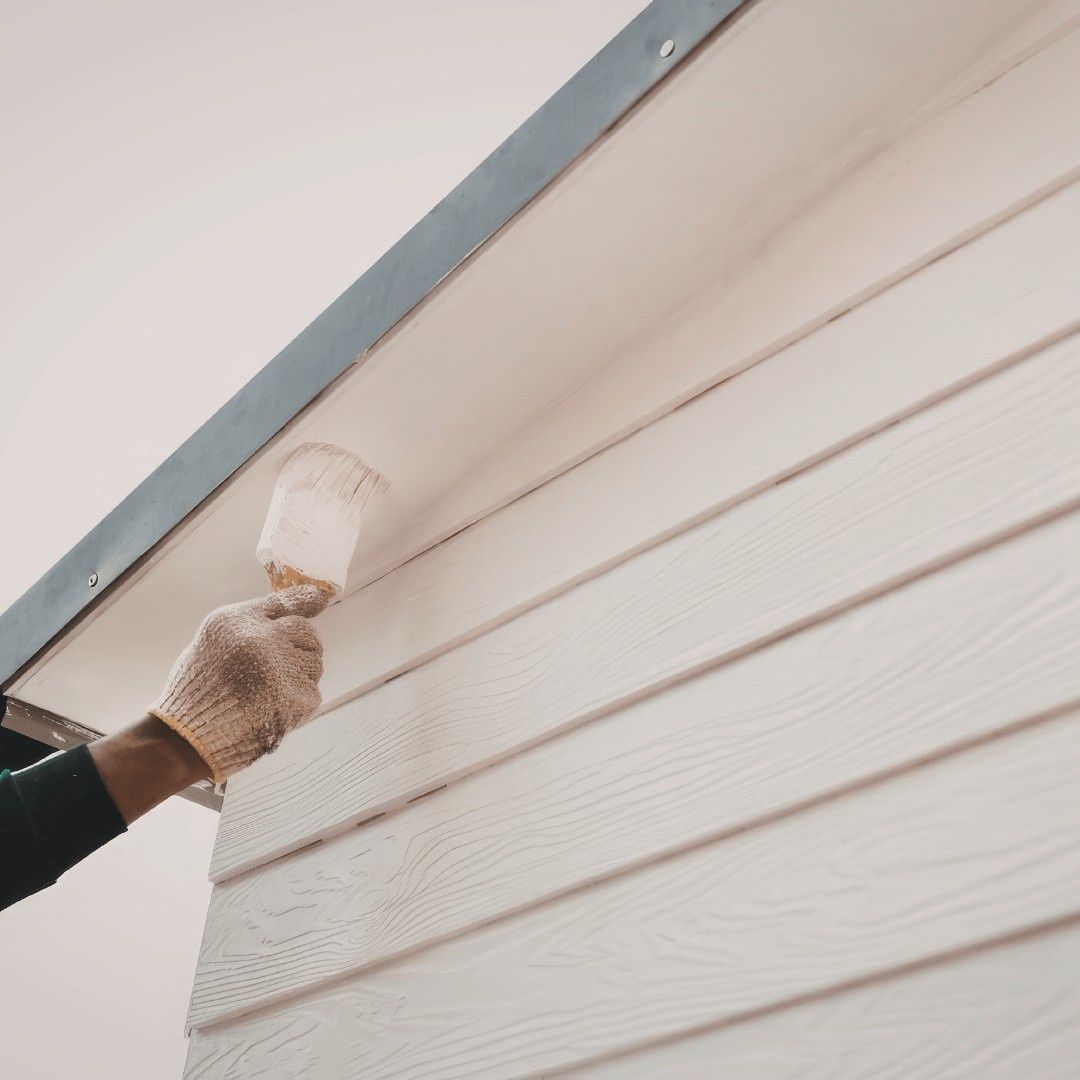 Gloved hand painting white siding with a brush outdoors