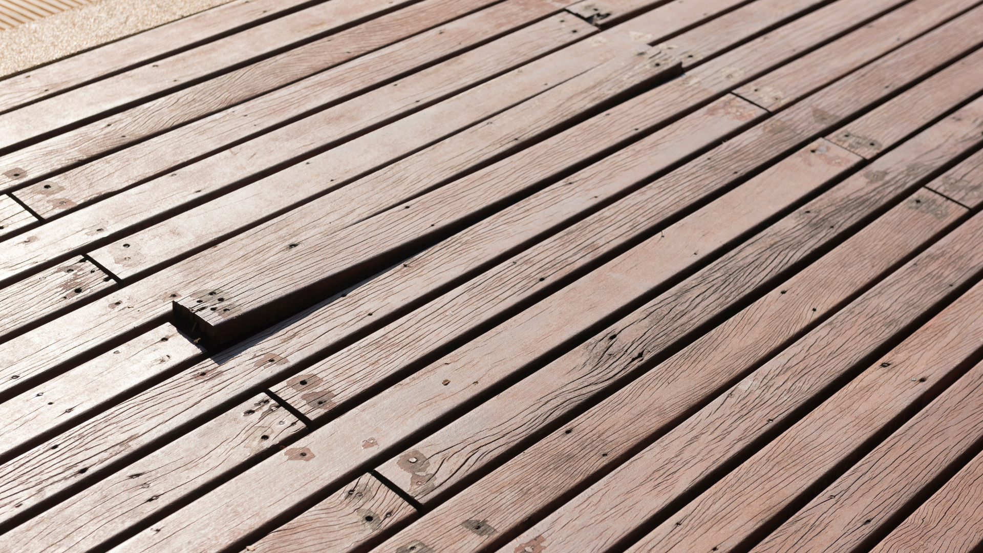 Hand applying varnish to a wooden deck, with one section already stained a warm orange-brown.
