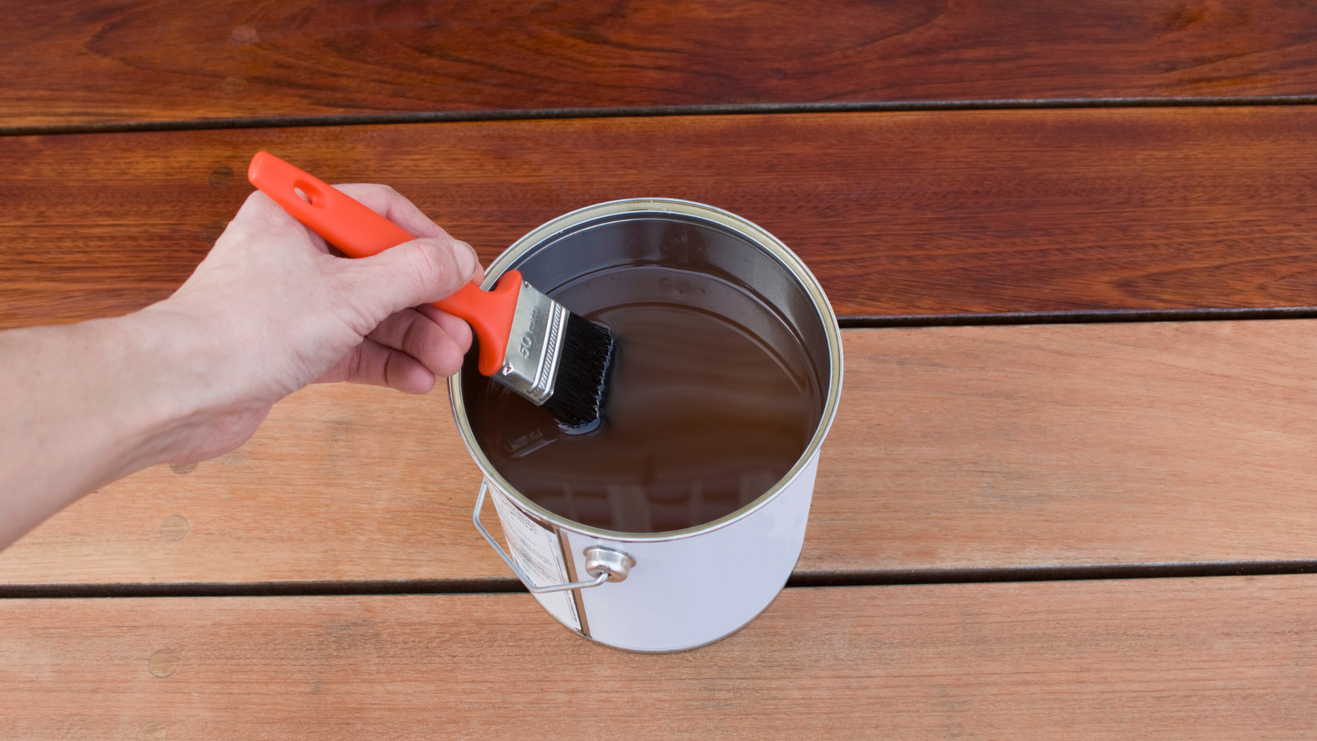 A hand painting the rim of a metal paint can with a brush on a wooden surface.