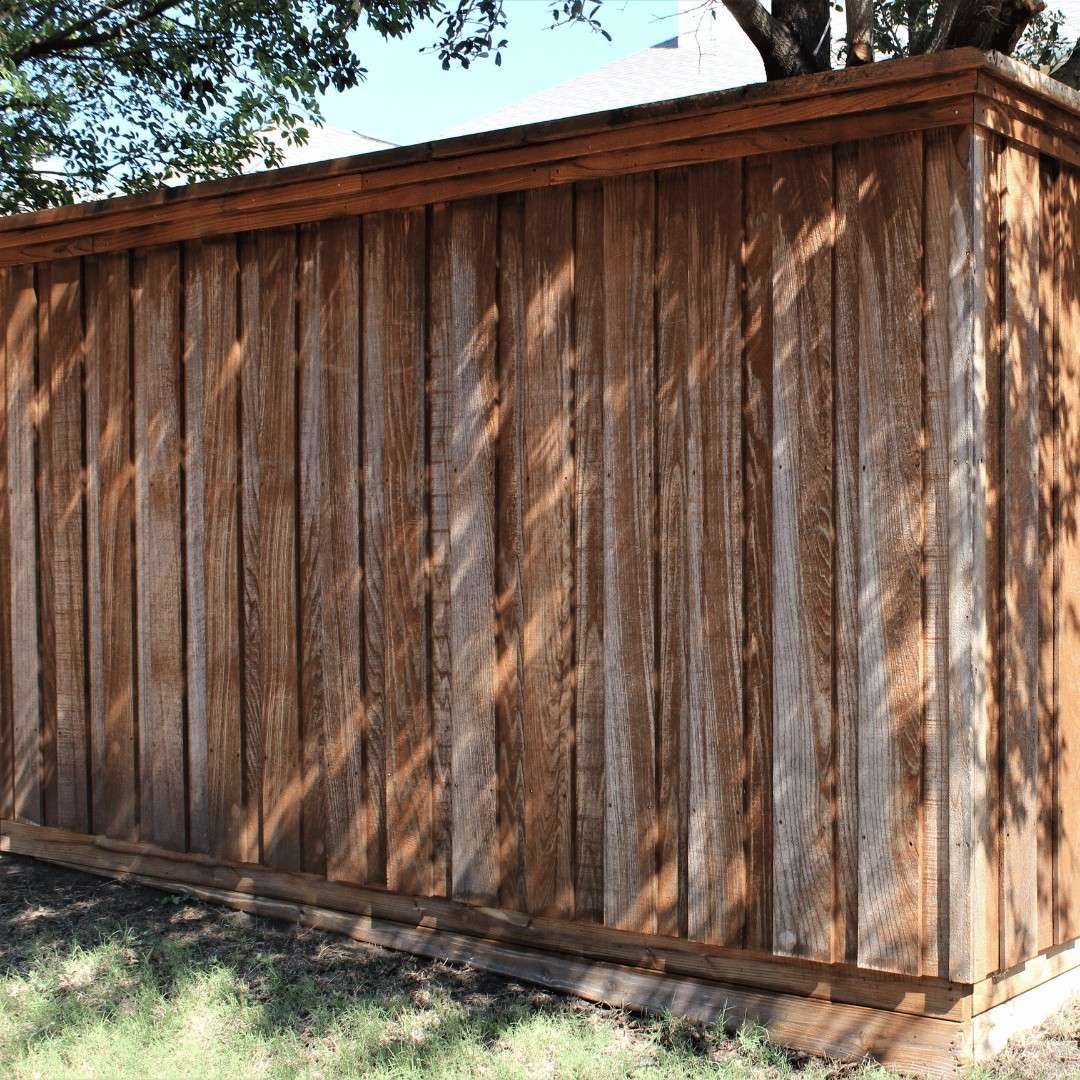 Hand applying varnish to a wooden deck, with one section already stained a warm orange-brown.