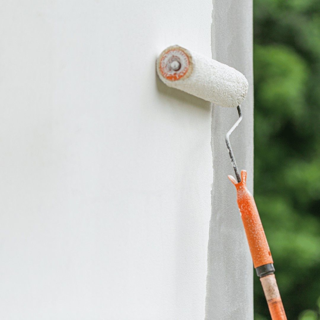 Paint roller with orange handle painting a white wall near a corner