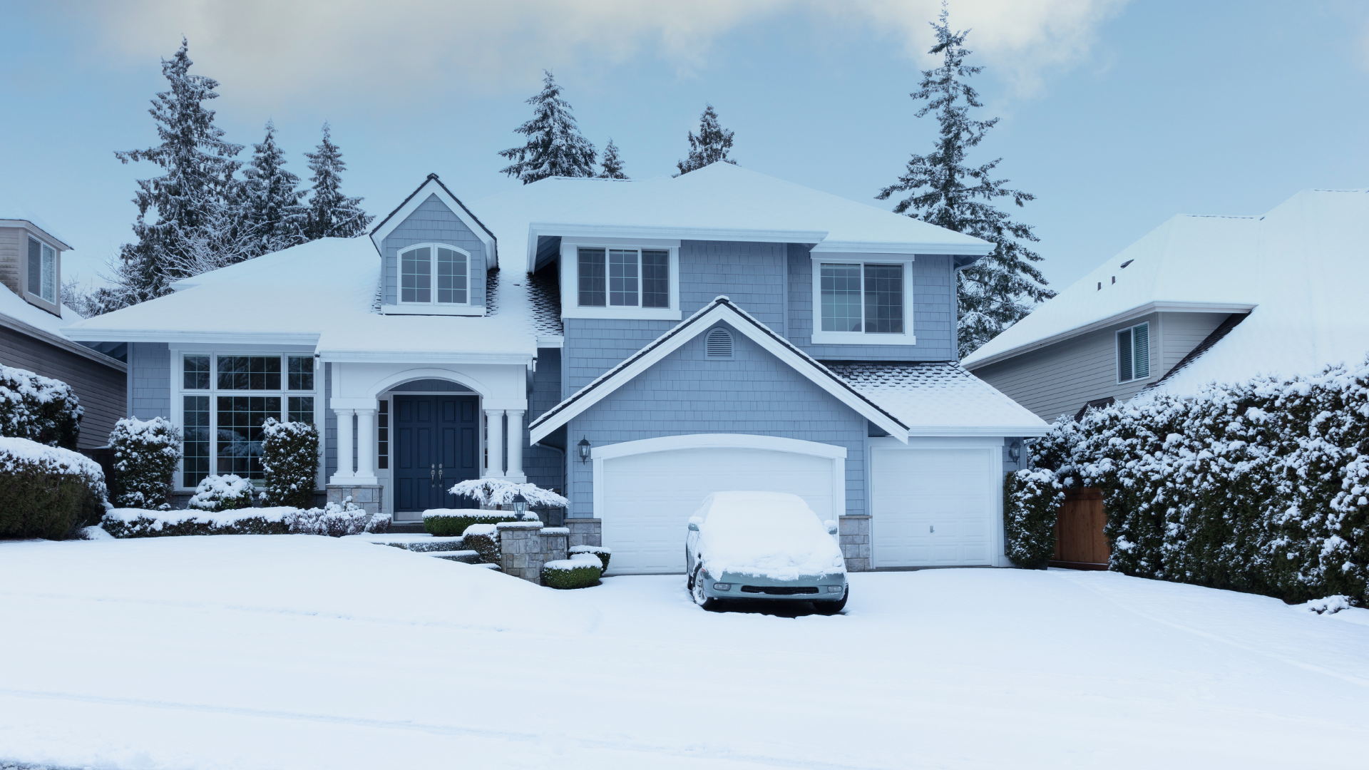 Snow-covered suburban house with a car buried in snow in the driveway