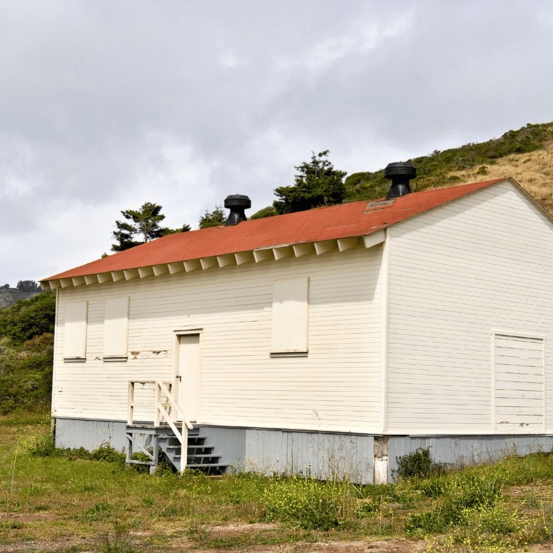 Small white house with a red roof on a grassy hillside under a cloudy sky
