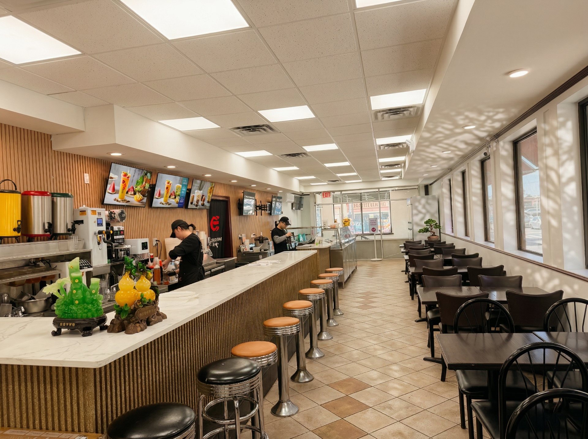 A modern, brightly lit restaurant interior featuring a long service counter with stools and dining tables along the wall.