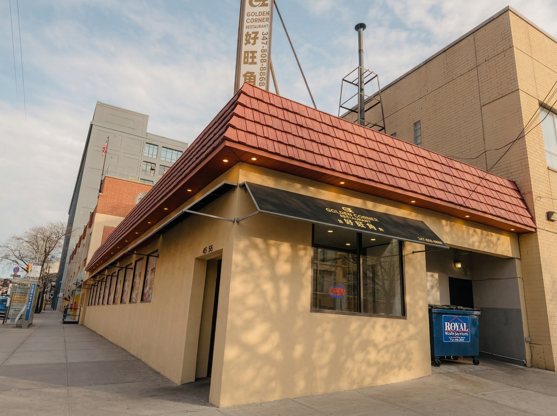 A beige, one-story commercial building on a corner with a red tiled mansard roof and a black awning over the window.