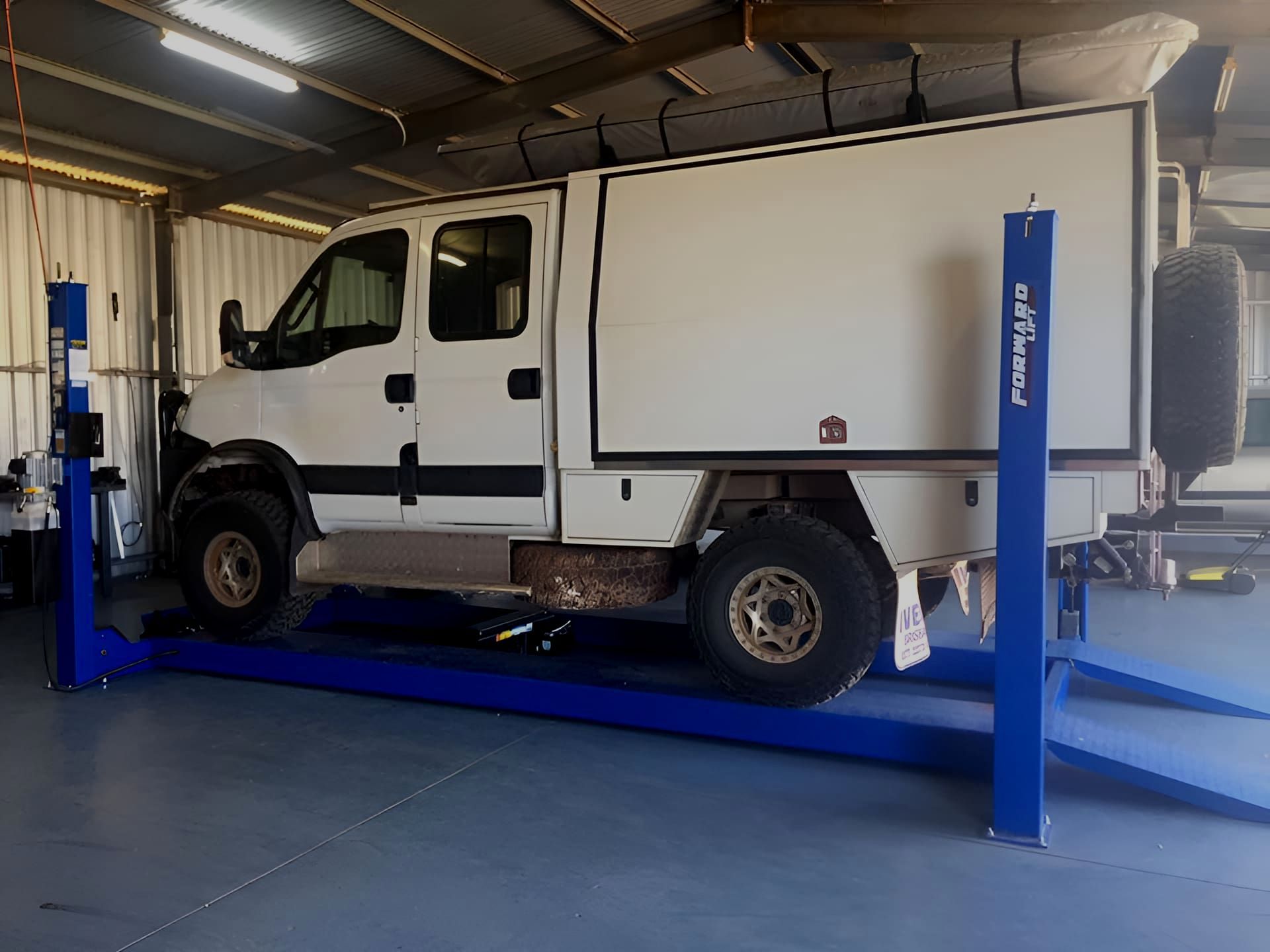 A White Truck Is Sitting On Top Of A Blue Lift In A Garage — Red Central Towing & Recovery In Alice Springs, NT